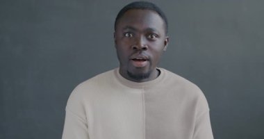 Heyecanlı Afrikalı Amerikalı adamın yavaş çekimde çekilmiş portresi. Kameraya bakıyor. Siyah arka planda mutlu ve şaşkın hissediyor.