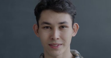 Gri arka planda kameraya gülümseyen mutlu Asyalı adamın yavaş çekim portresi. İnsanlar ve iyi ruh hali kavramı.