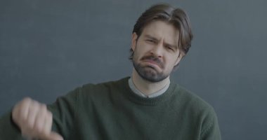 Siyah arka planda hayal kırıklığını ifade eden kameraya bakarak el hareketi yapan hoşnutsuz bir gencin portresi..