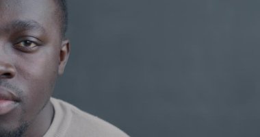 Siyah arka planda ciddi bir ifadeyle kameraya bakan Afro-Amerikan bir adamın yavaş çekim portresi. İnsanlar ve duygu kavramı.