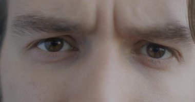 Erkek gözlerinin yavaş çekimde kameraya bakışları gergin bir şekilde bakarken erkek siyah arka planda endişeli hisseder..