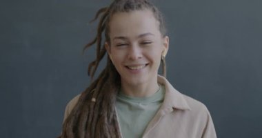 Rastalı mutlu genç bir kadının portresi çevrimiçi video görüşmesi yapıyor. Konuşuyor ve siyah arka planda kablosuz kulaklık kullanarak kameraya bakıyor..