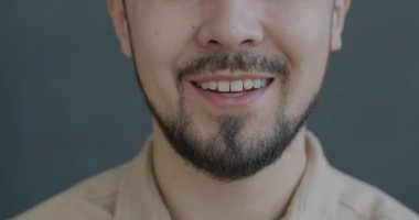 Gri arka planda neşeli hissederek gülen isimsiz bir gencin yavaş çekimleri. Mutluluk ve olumlu duygu kavramı.