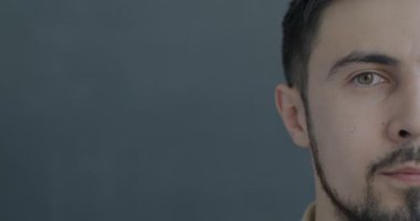 Melez bir adamın yarı yüzünün, gri arka planda duygusuz bir şekilde kameraya baktığı yavaş çekim portresi. İnsanlar ve ifade kavramı.