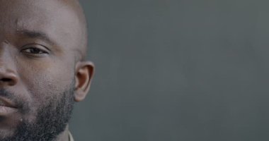 Ciddi bir Afro-Amerikan erkeğinin, duygusuz bir şekilde kameraya bakan yarım yüzünün yavaş bir portresi. Kendinden emin insanlar ve yüz ifadesi konsepti.
