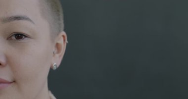 Gri arkaplanda kameraya bakarken gülümseyen neşeli Asyalı kadının yavaş çekim portresi. İnsanlar ve olumlu duygu kavramı.