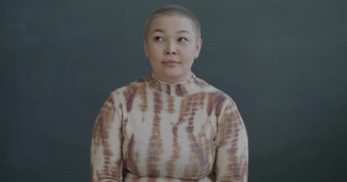 Düşünceli Asyalı kadının yavaş hareket eden portresi siyah arkaplandaki kameraya bakarak parmak kaldırıyor.