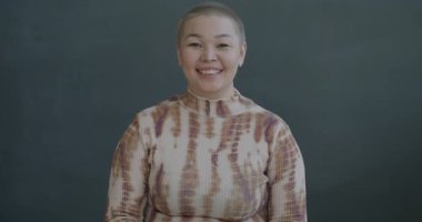 Siyah arka planda kameraya bakıp gülümseyen, el hareketi yapan mutlu Asyalı genç bayanın ağır çekim portresi.