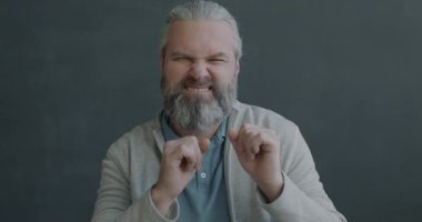 Neşeli, olgun bir adamın, kameraya bakıp, gri arka planda komik suratlar yaparak eğlendiği portresi. İnsanlar ve eğlence konsepti.