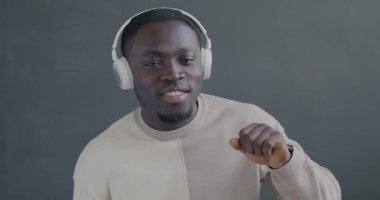 Kulaklıkla müzik dinleyen Afrikalı Amerikalı bir adam gri arka planda şarkı söylüyor. Gençlik kültürü ve eğlence kavramı.