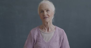 Kameraya bakan neşeli yaşlı kadının yavaş çekimde çekilmiş portresi siyah arka planda güzel bir sürprizle mutlu oluyor. İnsanlar ve olumlu duygu kavramı.