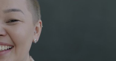 Gri arka planda kameraya bakarken eğlenen neşeli Asyalı yarım yüzlü kadının yakın plan portresi. İnsanlar ve mutluluk kavramı.