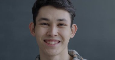 Gri arka planda kameraya bakıp gülen neşeli Asyalı adamın yakın plan portresi. İyi ruh hali ve mutlu insanlar konsepti.