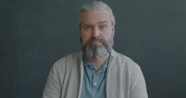 Gri arka planda kameraya bakan şaşırmış ve kafası karışmış olgun bir adamın yavaş çekim portresi. Olumsuz duygu ve insan kavramı.