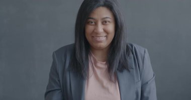 Siyah arkaplanda kameraya bakıp gülümseyen mutlu, melez bir kadının yavaş çekim portresi..