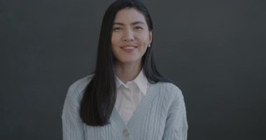 Dost canlısı Asyalı kadının gri arka planda kameraya el sallayarak gülümseyen portresi. İnsanlar ve jest konsepti.