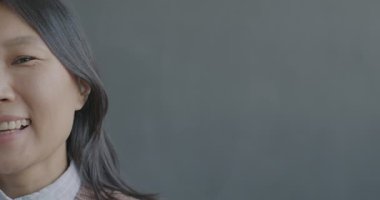 Siyah arka planda kameraya bakıp gülümseyen neşeli Asyalı kadının yavaş çekim portresi. Pozitif duygu ve insanların kavramı.