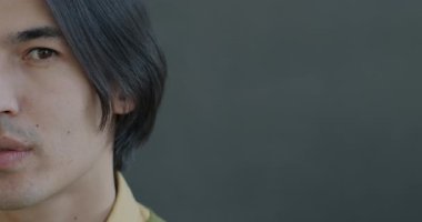 Gri arka planda kameraya bakan sakin Asyalı bir adamın yavaş çekim portresi. Duygu ve ifade kavramı.