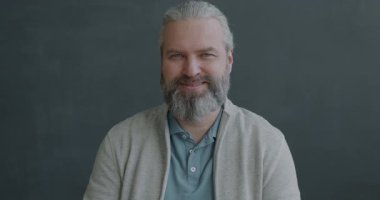 Dost canlısı, olgun bir adamın gri arka planda el sallayarak gülümsemesinin yavaş çekim portresi. İnsanlar ve ifade kavramı.