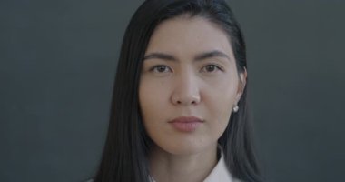 Kameraya bakan barışçıl Asyalı kadının yavaş çekimde çekilmiş portresi. Siyah arka planda kendine güvenen. İnsanlar ve yüz ifadesi kavramı.