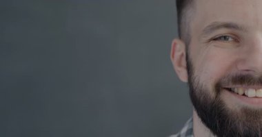 Gri arkaplandaki kameraya bakıp gülen neşeli, yarım yüzlü bir gencin yakın plan portresi. İnsanlar ve olumlu duygu kavramı.