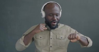 Siyah arka planda dans eden, kulaklıklı müzik dinleyen Afrikalı Amerikalı adamın yavaş çekimleri. İnsanlar ve eğlence konsepti.