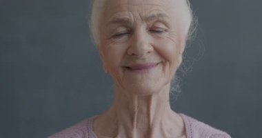 Kameraya gülümseyen, siyah renkli arka planda mutlulukla gülümseyen neşeli yaşlı kadının yavaş hareket eden portresi. İnsanlar ve olumlu duygu kavramı.