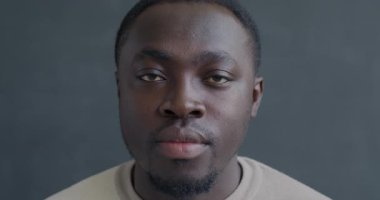 Close-up slow motion portrait of serious African American man looking at camera with no emotion on black color background. People and face expression concept.