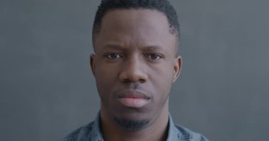 Siyah arka planda kameraya bakan kasvetli Afrikalı Amerikalı adamın yavaş çekim portresi. İnsanlar ve olumsuz duygu kavramı.