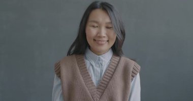 Tatmin olmuş Asyalı bir kadının, siyah arka planda kameraya bakıp gülümseyen el hareketi..