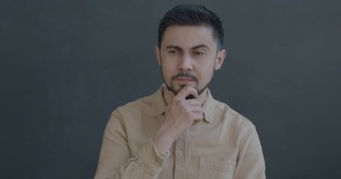 Düşünceli, melez bir adamın yavaş hareket eden portresi. Sonra parmağını kaldırıp gri arka plandaki kameraya bakmak harika bir fikir.