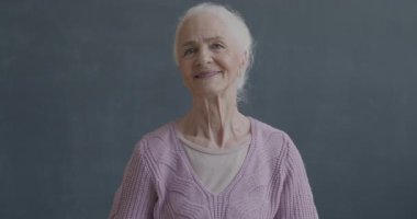 Siyah arka planda kameraya gülümseyerek gülümseyen mutlu yaşlı bayanın yavaş çekim portresi. İnsanlar ve olumlu duygu kavramı.