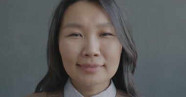 Kameraya bakıp gülümseyen neşeli Asyalı kadının yavaş çekim portresi. Neşeli insanlar ve olumlu duygu kavramı.