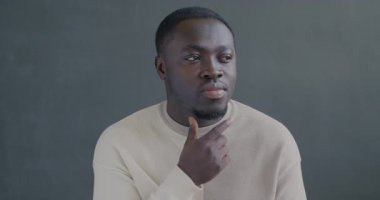 Düşünen Afrikalı Amerikalı adamın yavaş hareket eden portresi parmak kaldırmayı düşünen gri arkaplandaki kameraya bakan fikri olan.