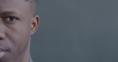 Siyah arka planda duygusuz bir şekilde kameraya bakan Afrikalı Amerikalı bir adamın yavaş çekim portresi..