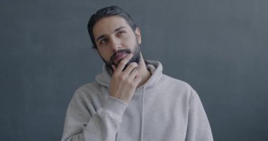 Düşünceli Orta Doğulu bir adamın yavaş hareket eden portresi. Sonra parmağını kaldırıyor. Gri arkaplandaki kameraya bakıyor..