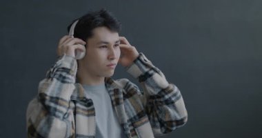 Neşeli Asyalı adam kulaklık takıyor müzik dinliyor ve gri arka planda dans ediyor. Modern teknoloji ve eğlence konsepti.