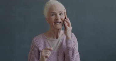 Cep telefonuyla konuşan mutlu yaşlı bir kadının yavaş çekimde çekilmiş portresi siyah arka planda sohbetin keyfini çıkarıyor. İnsanlar ve iletişim konsepti.
