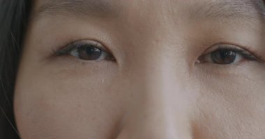 Güzel Asyalı genç kadın gözlerinin duygusuz bir şekilde kameraya bakışının yavaş çekim portresi. Yüz ifadesi ve insanların konsepti.