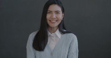 Siyah arka planda kameraya bakarak el hareketi yapan neşeli Asyalı kadının yavaş çekim portresi..