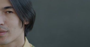 Gri arka planda gülümseyen kameraya bakan mutlu Asyalı adamın yavaş çekim portresi. Olumlu duygu ve neşeli insan konsepti.