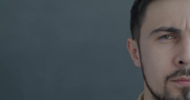 Gri arka planda kameraya bakan endişeli melez bir adamın yavaş çekim portresi. İnsanlar ve olumsuz duygu kavramı.