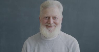 Siyah arkaplanda kameraya bakıp gülümseyen mutlu yaşlı bir adamın yavaş çekim portresi..