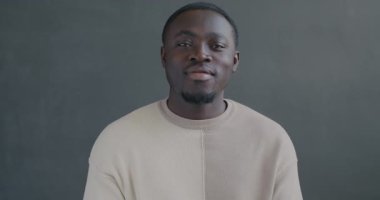 Siyah arka planda kameraya bakıp gülümseyen mutlu Afro-Amerikalı adamın yavaş hareket eden portresi.