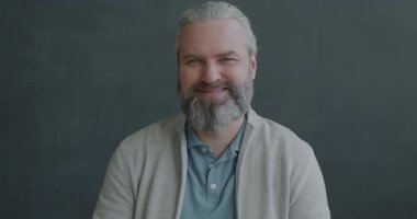 Olgun bir adamın, gri arka planda kameraya gülümseyen el hareketi gösteren mutlu bir portresi. İnsanlar ve duygu kavramı.