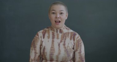 Kameraya bakan heyecanlı genç Asyalı kadının yavaş çekimde çekilmiş portresi. Siyah arka planda şaşkın ve sevinç dolu.