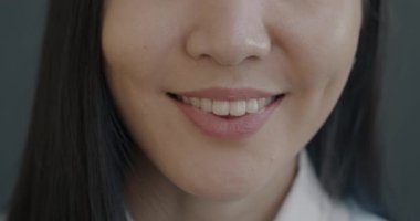 Gri arka planda gülümseyen neşeli, genç kadın dudaklarının yavaş çekim portresi. İnsanlar ve olumlu duygu kavramı.