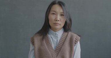 Mutsuz Asyalı kadının yavaş hareket eden portresi baş aşağı el hareketi yapıyor ve siyah arkaplanda kameraya bakıp başını sallıyor..