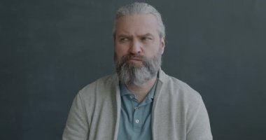 Düşünceli olgun bir adamın yavaş hareket eden portresi. Sonra parmağını kaldırıyor. Siyah arka planda kameraya bakıp gülümsüyor.