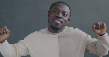 Gri arka planda kameraya bakarak dans eden mutlu Afrikalı Amerikalı adamın yavaş çekim portresi. Eğlence ve insan konsepti.